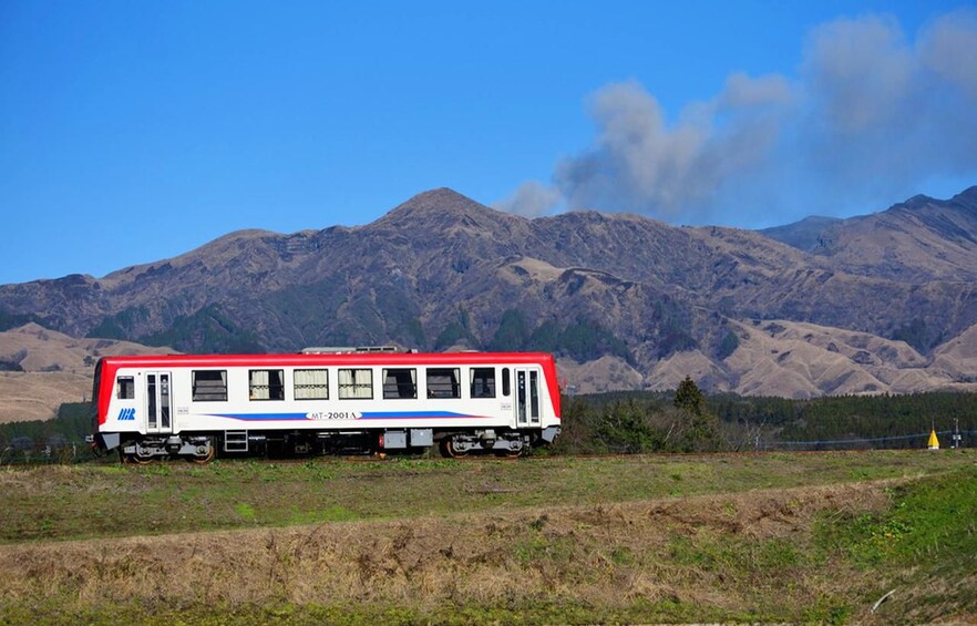 A red and white train with 'MT-2001' on the side, traveling on tracks with a mountainous landscape in the background. 3