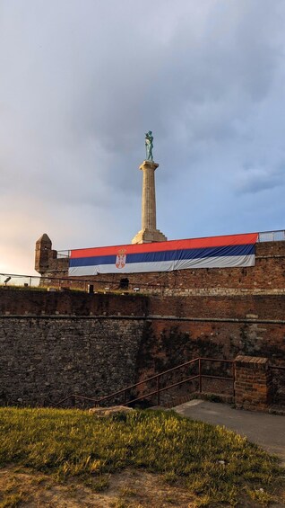 A monument with a flag, a stone wall, and a grassy area. 1