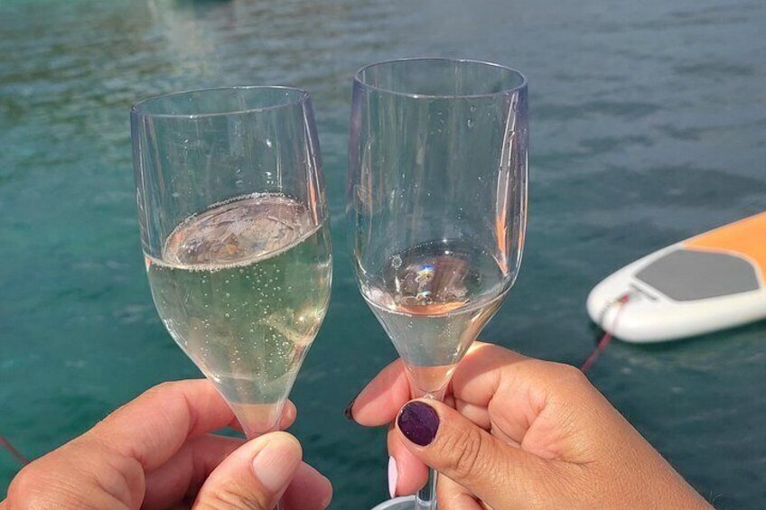 Dos manos sosteniendo copas de vino, con un barco al fondo. 3