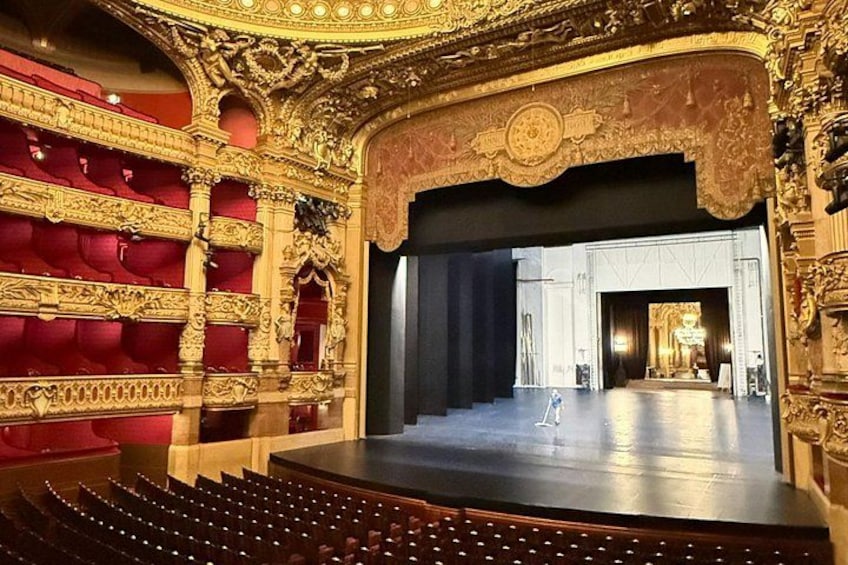 An ornate theater interior with red velvet seating and a stage. 1