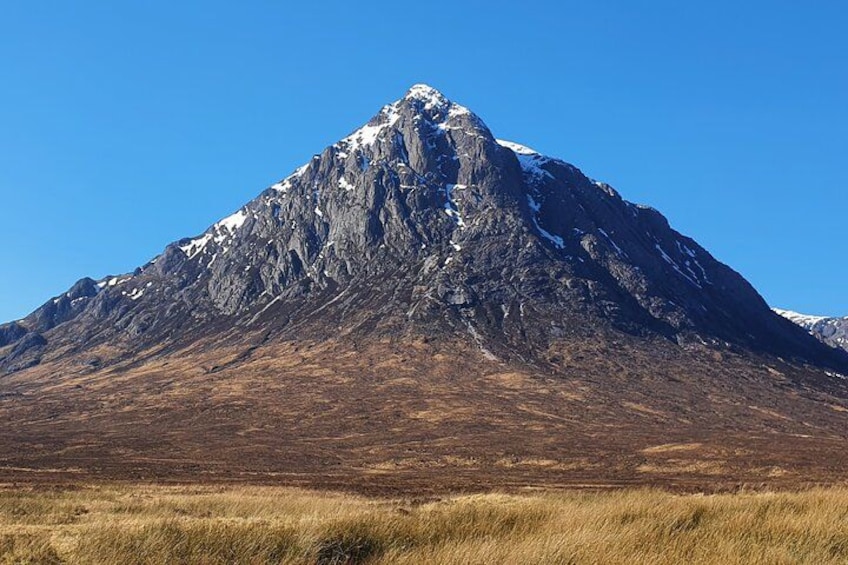 A mountain with a snow-capped peak, a clear blue sky, and a grassy foreground. 2