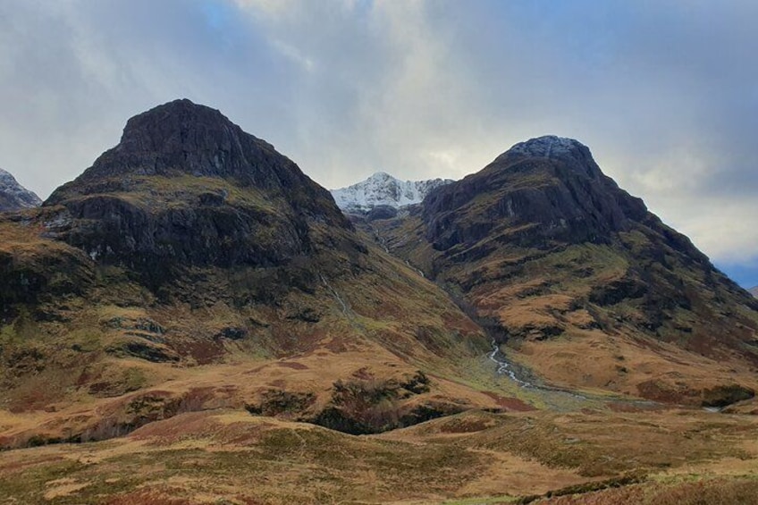 A mountainous landscape with two prominent peaks, a valley, and a stream. 3