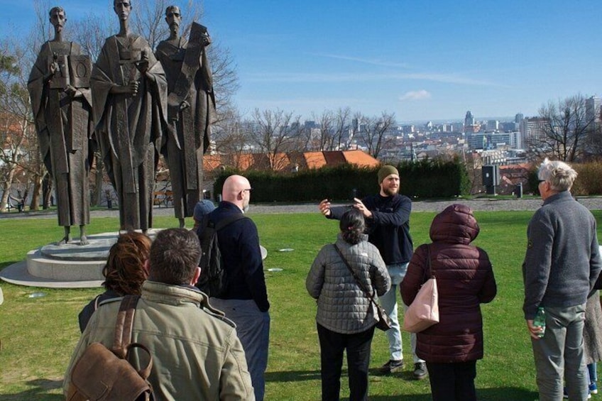 A group of people standing in a park with a statue in the foreground and a cityscape in the background. 4