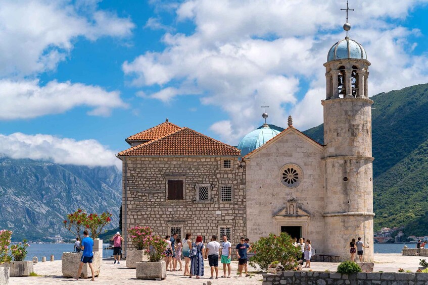 A historic stone building with a bell tower and a dome, surrounded by tourists. 1