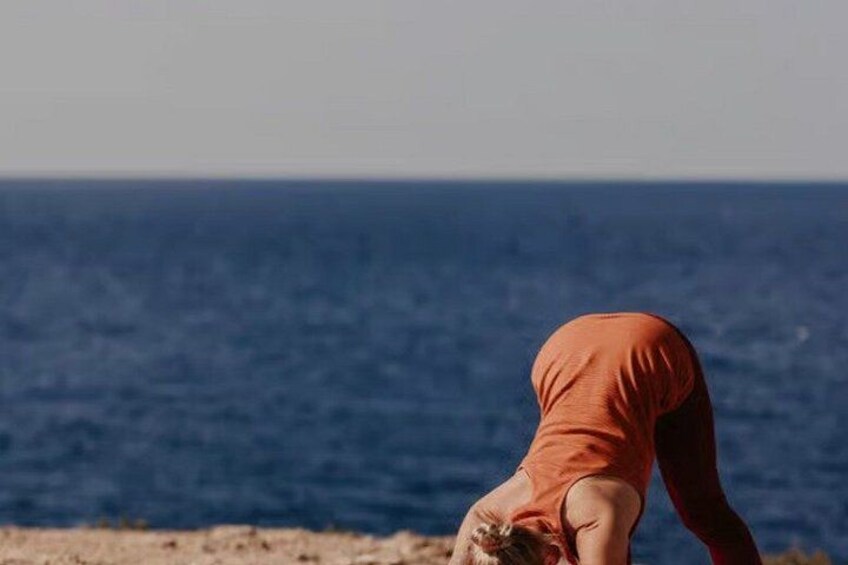 A person in an orange top performing a yoga pose on a beach with the ocean in the background. 3
