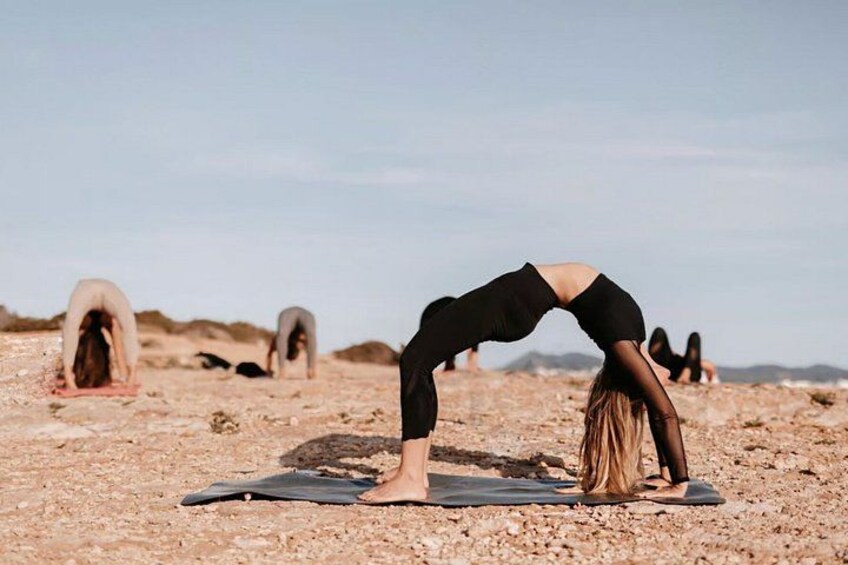 A person performing a yoga pose on a mat in a rocky outdoor setting. 2