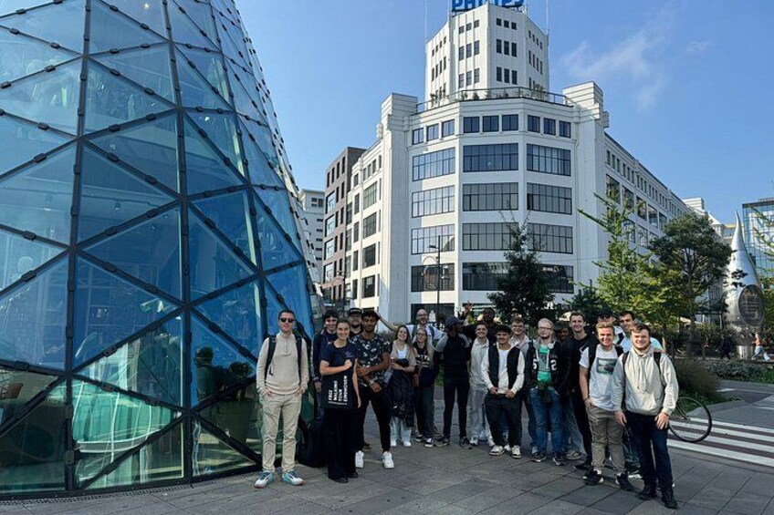 A group of people standing in front of a modern glass building and a white office building. 3