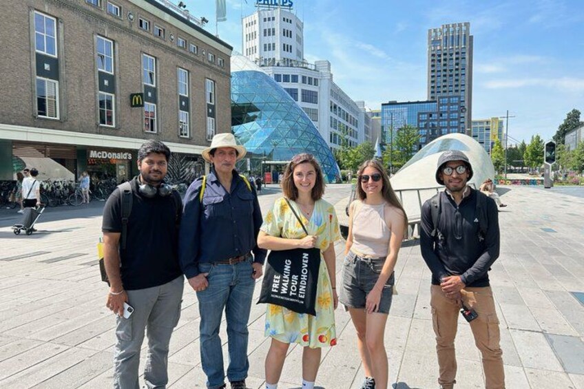 Un groupe de personnes se tient sur une place publique, avec des immeubles et un restaurant McDonald's en arrière-plan. 3