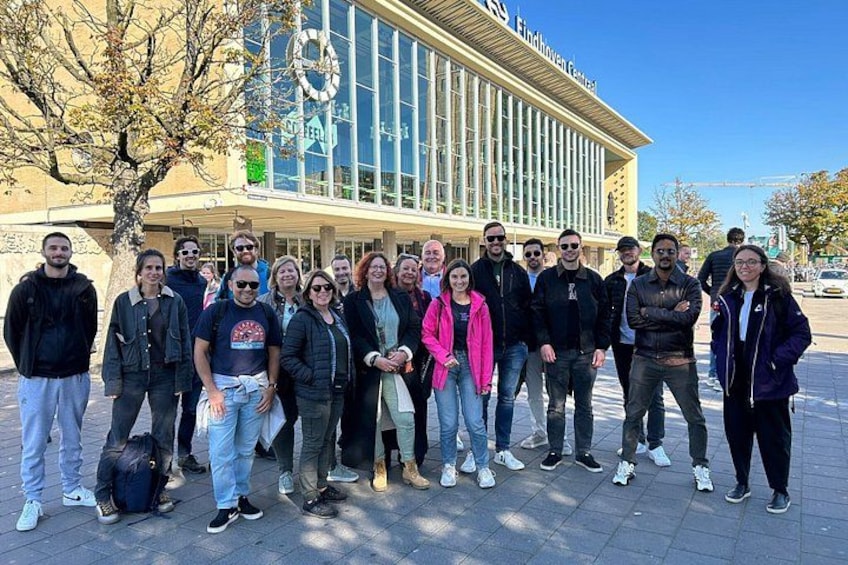 A group of people standing in front of a building with a large circular sign and a glass facade. 5