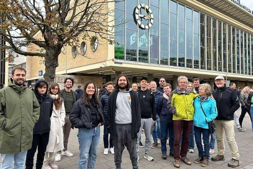 A group of people standing in front of a building with a large clock and a sign that reads 'COFFEE'. 4