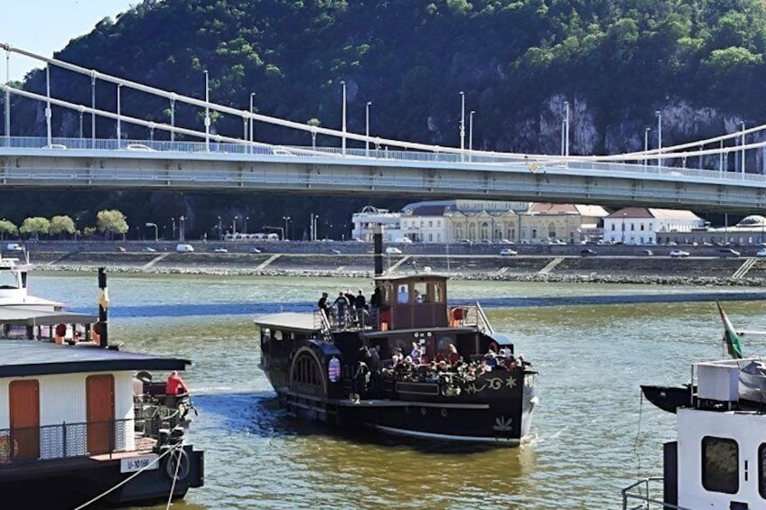 Un fiume con un ponte sullo sfondo, una barca con passeggeri e edifici lungo la riva. 5