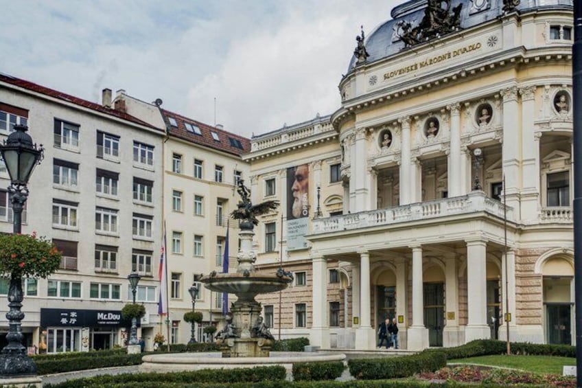 Un edificio storico con architettura classica, una fontana e un ristorante McDonald's in primo piano. 2