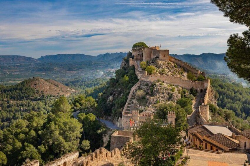 Un'antica fortezza in pietra su una collina, circondata da vegetazione e con montagne sullo sfondo. 1
