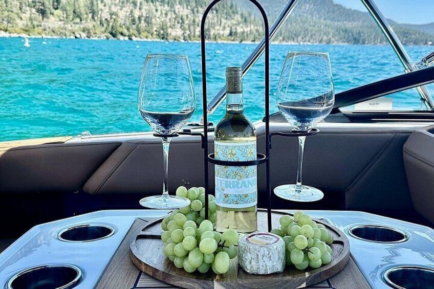 A boat with a table set for a meal, featuring a bottle of wine, two wine glasses, and a bowl of grapes. 5