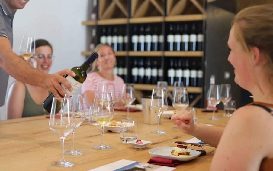 A group of people at a wine tasting event with wine glasses and bottles on a wooden table. 4