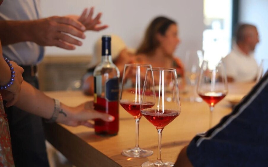 A group of people at a table with wine glasses and a bottle of red wine. 1