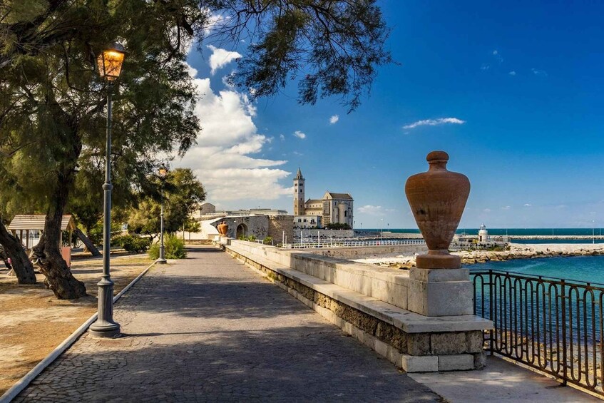 A coastal walkway with a large vase, trees, and a distant building with a tower. 5