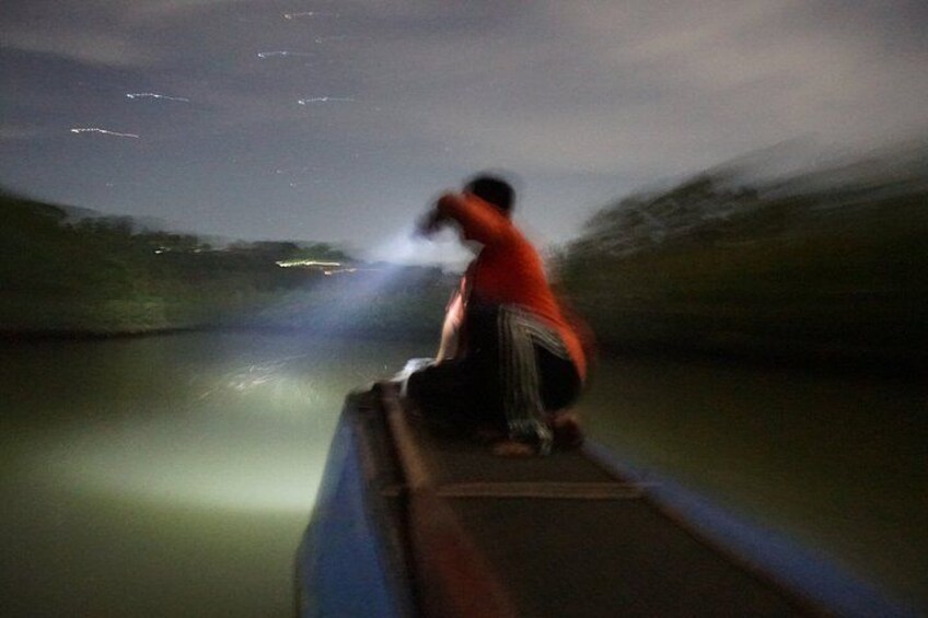 A person in a red shirt and striped shorts on a boat, holding a flashlight. 1