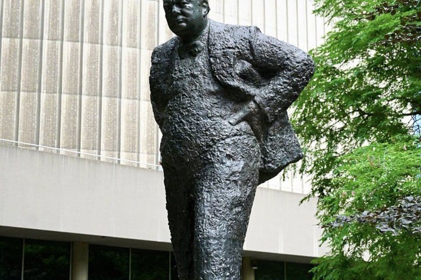 Una statua di un uomo in giacca e cravatta, in piedi all'aperto con un edificio sullo sfondo. 2