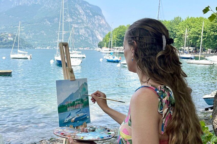 A person painting a landscape with a mountain and boats in the background. 5