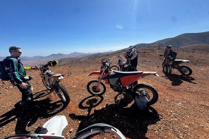 A group of people on dirt bikes in a barren landscape with mountains in the background. 3