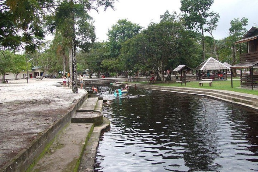A calm water body with a wooden dock, surrounded by trees and a few people. 3