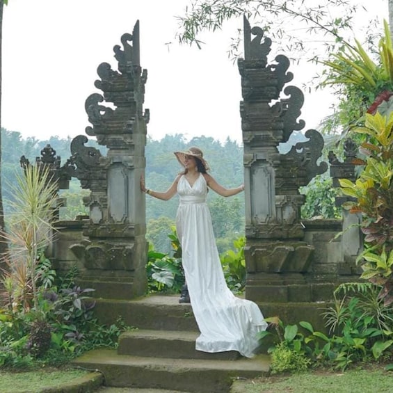 A woman in a white dress standing between ornate stone pillars with a lush garden and mountainous backdrop. 5