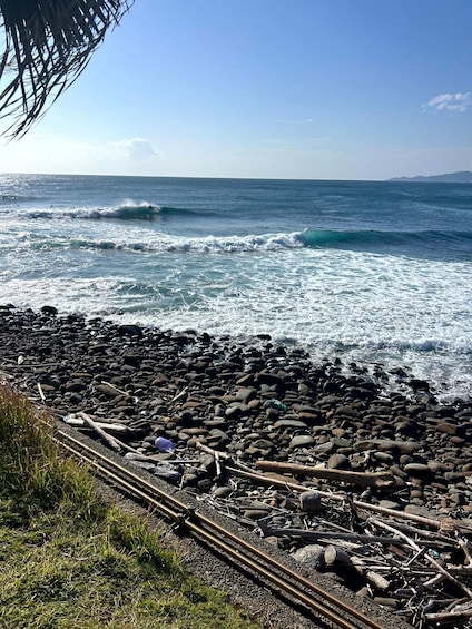 A rocky shoreline with waves crashing onto the beach and a clear blue sky above. 2