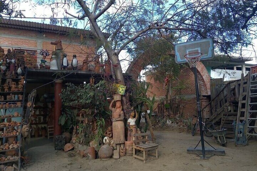 A rustic outdoor setting with a basketball hoop, wooden sculptures, and a variety of plants. 3