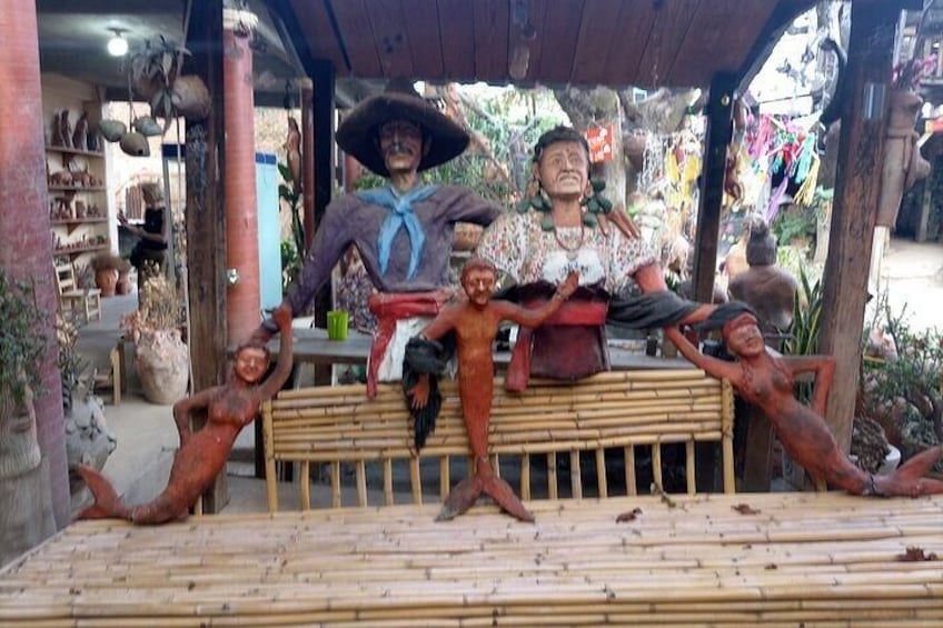 Un banco de madera con una escultura de una figura con un sombrero grande y una figura con aspecto infantil. 3