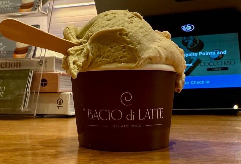 A cup of gelato with a wooden spoon, labeled 'BACIO di LATTE GELATO PURO,' in a setting with a digital screen displaying 'COCO RIO' and 'Royalty Points.' 4