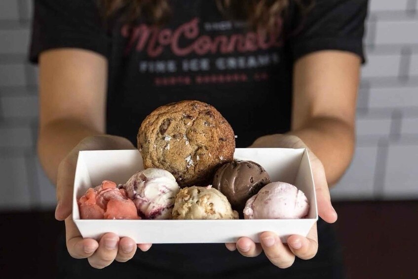 A person holding a box containing a muffin and various ice cream flavors. 1