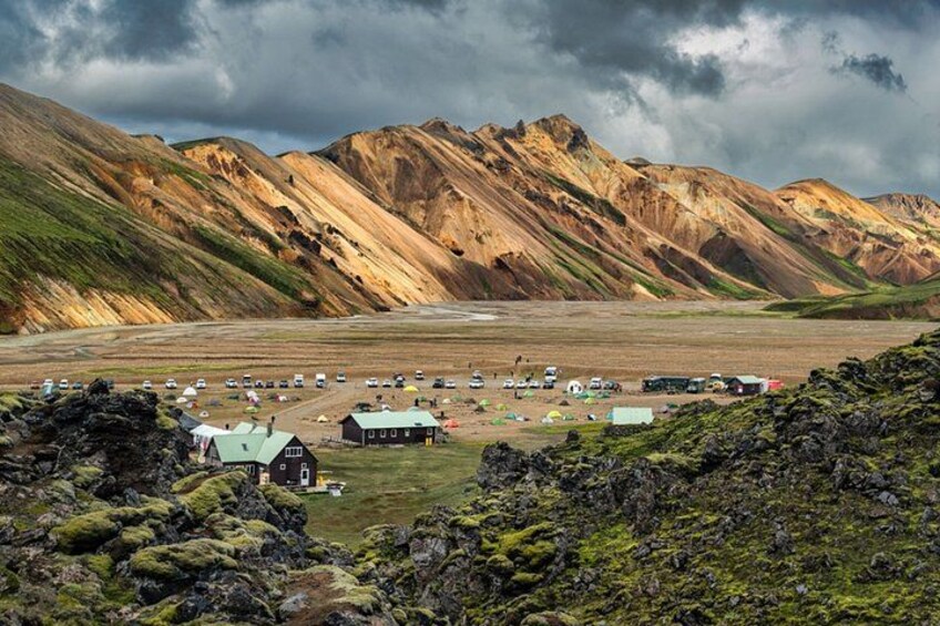 A mountainous landscape with a small settlement, including buildings and parked vehicles. 3