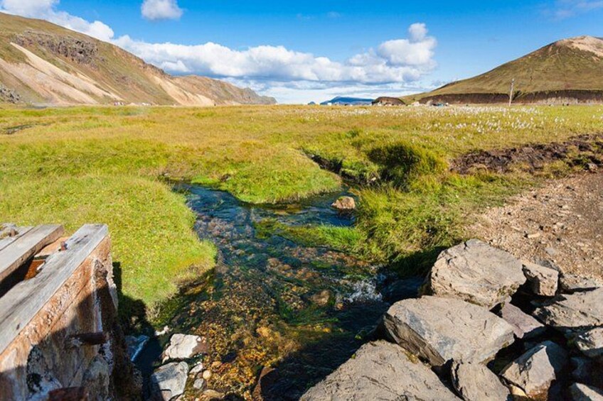A clear stream with rocks, grassy banks, and distant hills. 4