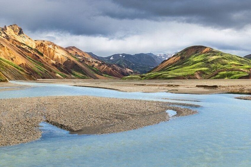 A river with pebbly banks, mountains in the background, and a cloudy sky. 2