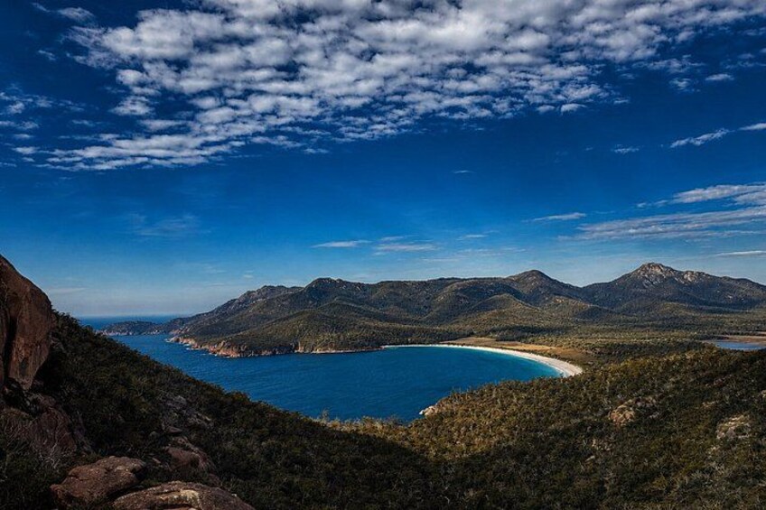 A coastal landscape with a clear blue sea, a sandy beach, and a mountainous backdrop under a partly cloudy sky. 3