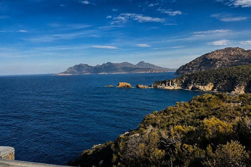A coastal landscape with a clear blue sea, rocky terrain, and distant mountains. 2
