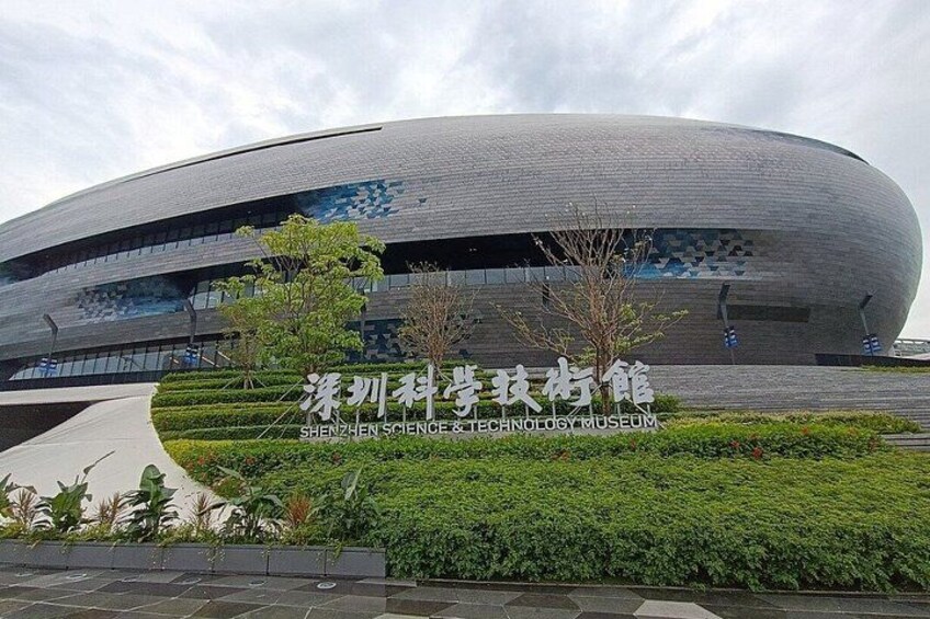 A modern building with a curved facade, surrounded by well-maintained greenery and a clear sky. 2