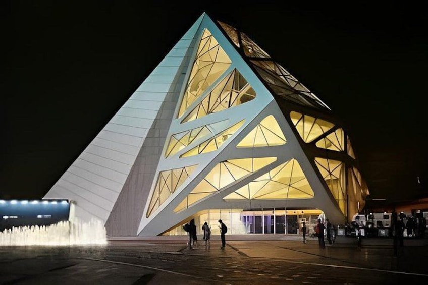 A modern building with a triangular facade and a fountain in the foreground. 3