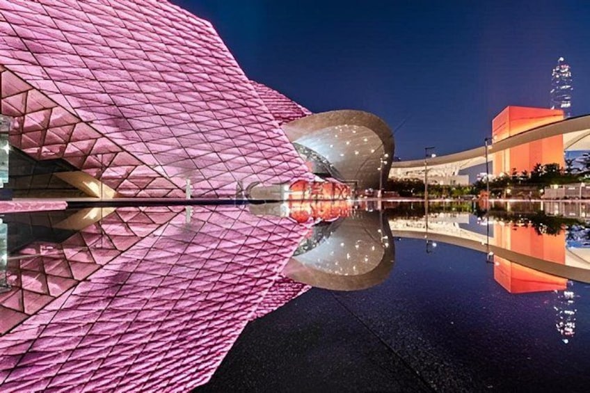 A pink building with a unique geometric design, a large reflective surface, and a clear reflection in the water. 5