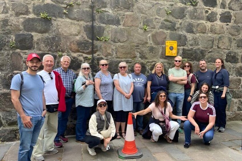 A group of people posing in front of a stone wall with a yellow sign. 2