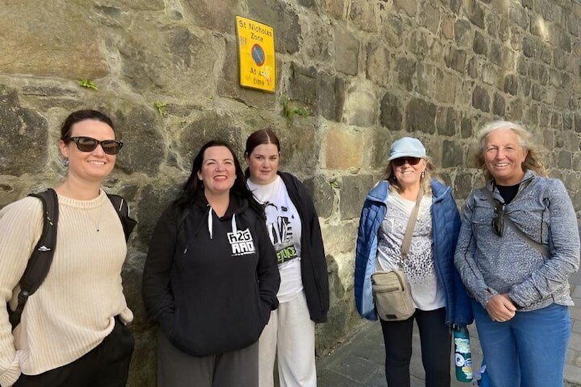 Four people standing in front of a stone wall with a yellow sign. 2