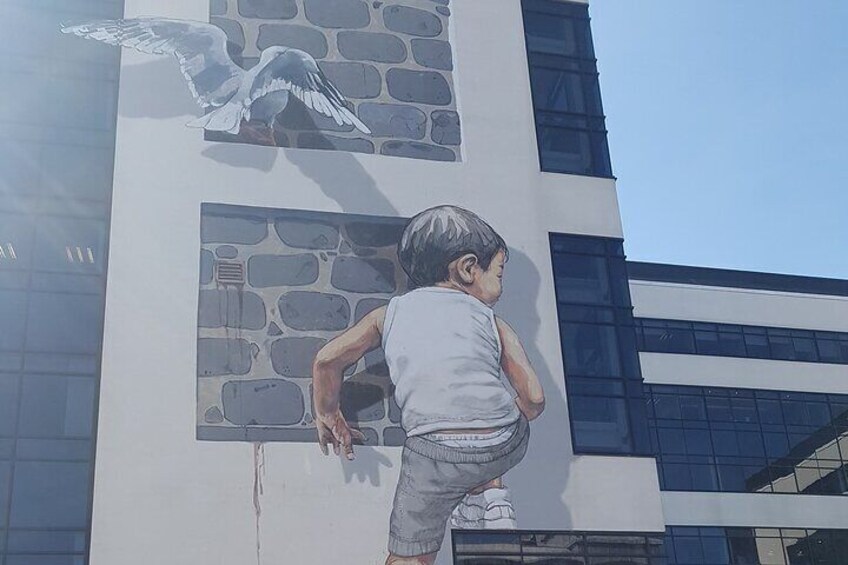 A child climbing a wall with a mural of a dove and a boy. 1