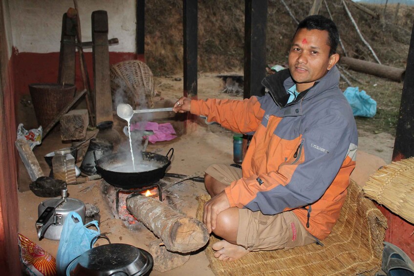 A person cooking over an open fire with a pan, surrounded by cooking utensils and a makeshift stove. 3