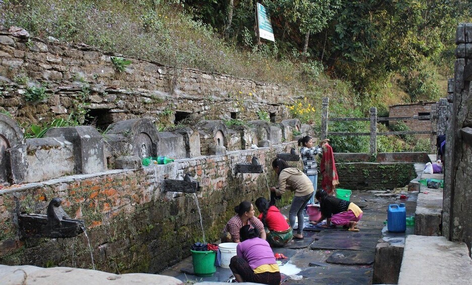 People washing clothes by a stone wall with water spouts. 2