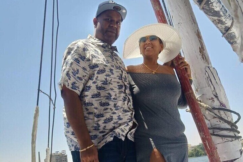 A person wearing a floral shirt and a woman in a gray dress standing on a boat with a red mast. 3