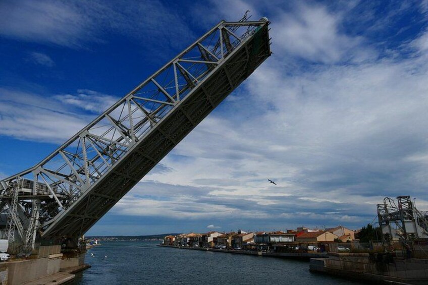 A large metal bridge spanning a body of water, with buildings and a clear sky in the background. 3