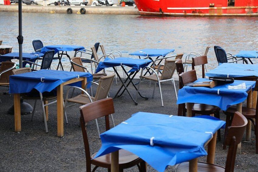 Outdoor tables with blue tablecloths and wicker chairs by a waterfront. 2