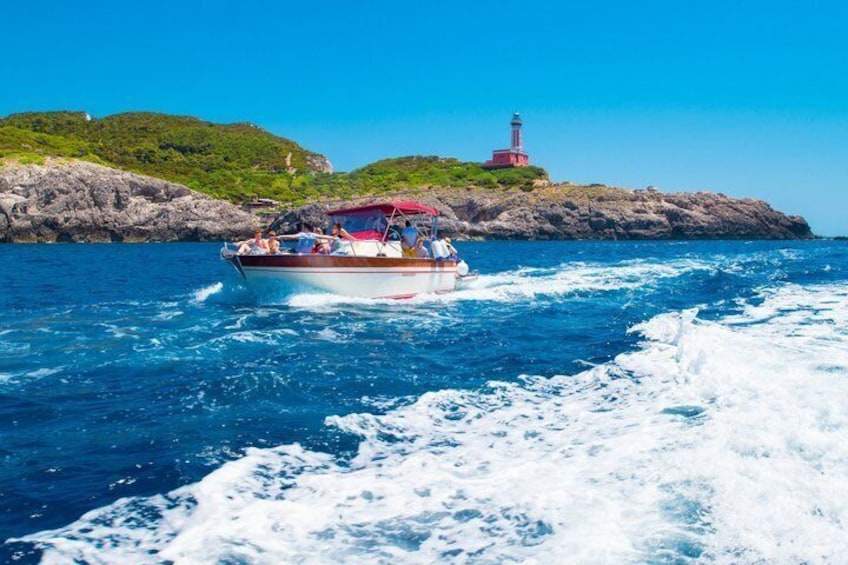 Una barca con passeggeri in una giornata limpida, una costa rocciosa e un faro sullo sfondo. 3