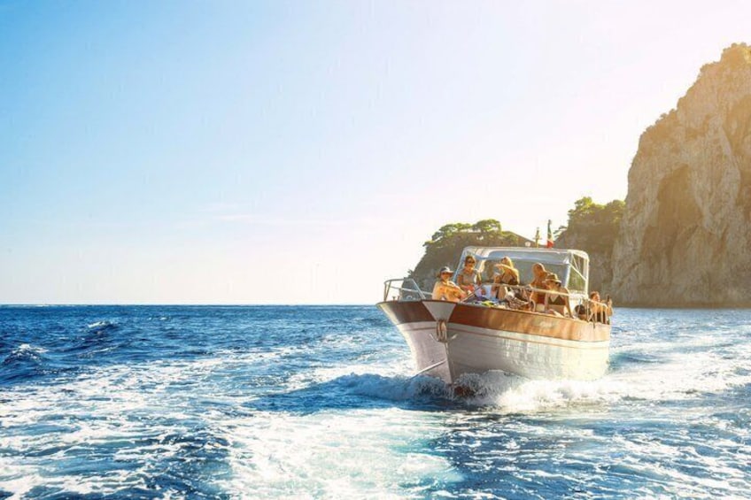 Una barca con passeggeri che naviga in acque blu, con una costa rocciosa sullo sfondo. 4